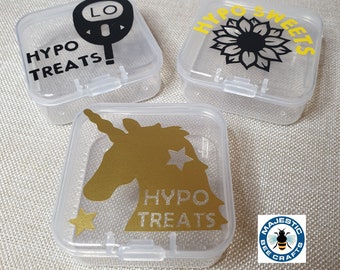 May include: Three clear plastic square containers with lids. Each container has a different design on the top. One container has a black and yellow design with the text "Hypo Treats" and a black silhouette of a blood glucose meter. Another container has a black and white sunflower design with the text "Hypo Sweets". The third container has a gold unicorn design with the text "Hypo Treats".