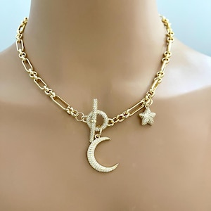 May include: Gold chain necklace with a toggle clasp and two charms: a crescent moon and a star. Both charms are encrusted with clear rhinestones.