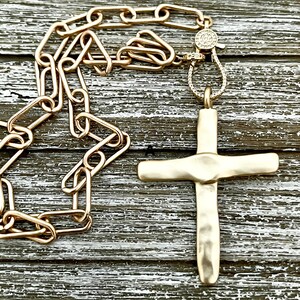 May include: A gold chain necklace with a hammered gold cross pendant. The chain has a diamond-encrusted clasp. Also available in matte gold.