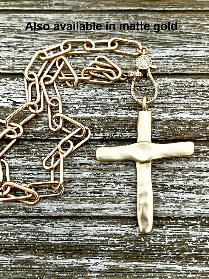 May include: A gold chain necklace with a hammered gold cross pendant. The chain has a diamond-encrusted clasp. Also available in matte gold.