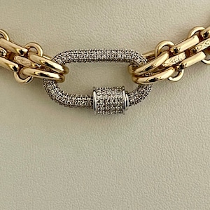 May include: A gold chain necklace with a large oval-shaped clasp set with small clear stones. The clasp is made of two interlocking pieces.