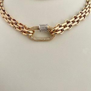 May include: A gold chain necklace with a large oval-shaped clasp set with small clear stones. The chain is made of two different styles of links.