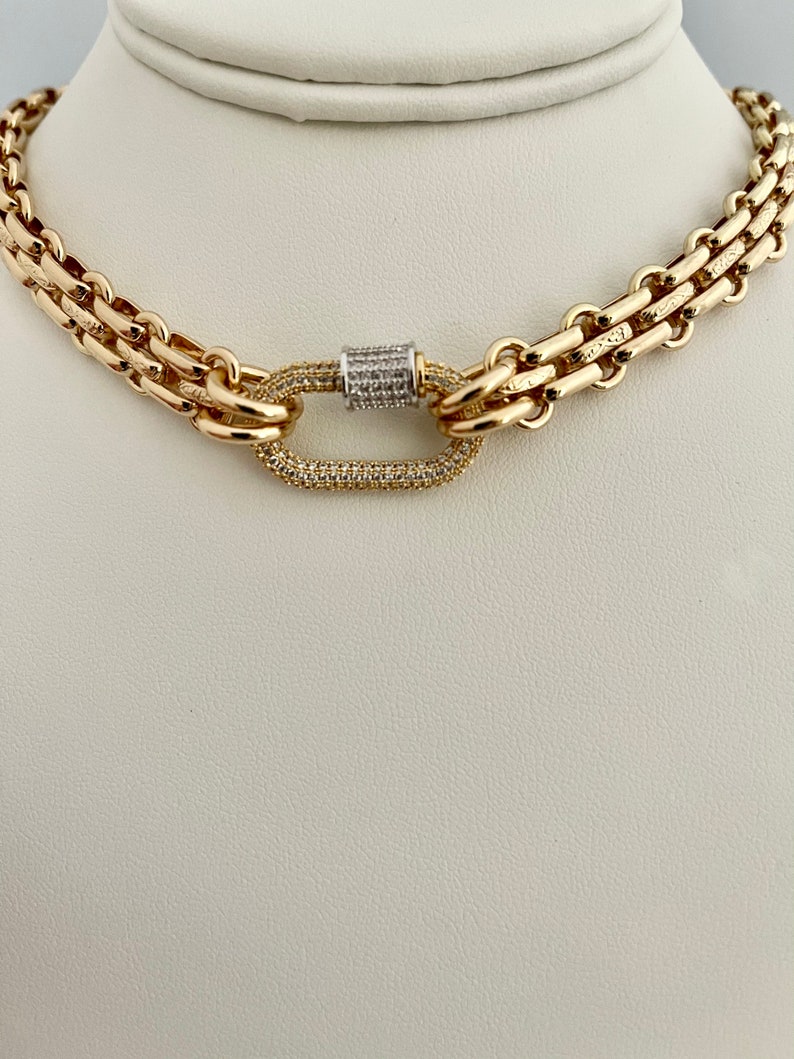 May include: A gold chain necklace with a large oval-shaped clasp set with small clear stones. The chain is made of two different styles of links.