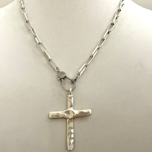 May include: A silver chain necklace with a hammered silver cross pendant. The chain has a small, round, pave-set diamond clasp.