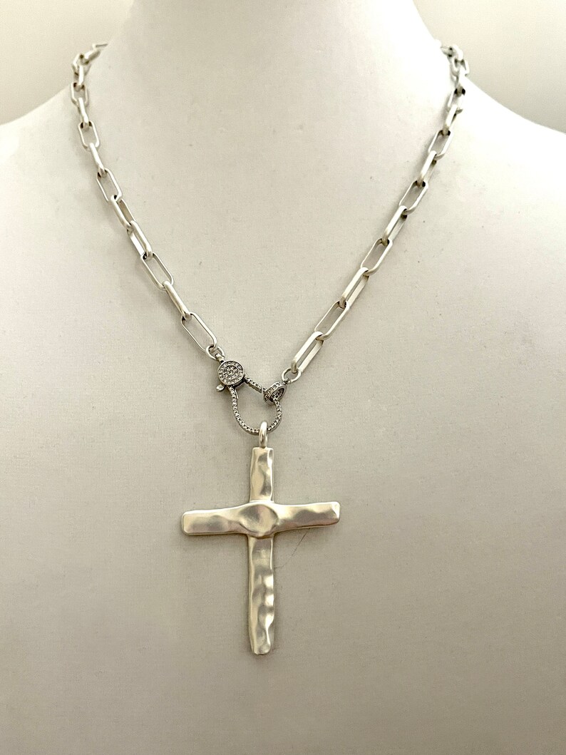 May include: A silver chain necklace with a hammered silver cross pendant. The chain has a small, round, pave-set diamond clasp.