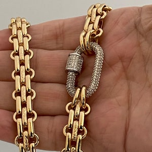 May include: A gold chain necklace with a large, oval-shaped clasp set with clear stones. The chain is made of multiple rows of linked gold pieces.