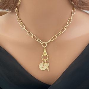 May include: Gold-toned necklace featuring a chain link design. The pendant includes a lock and key charm, both encrusted with small, sparkling stones. The necklace is a statement piece, perfect for adding a touch of elegance to any outfit.