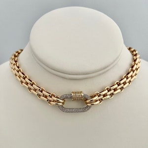 May include: A gold chain necklace with a large, oval-shaped clasp set with small diamonds. The chain is made of multiple strands of linked metal.