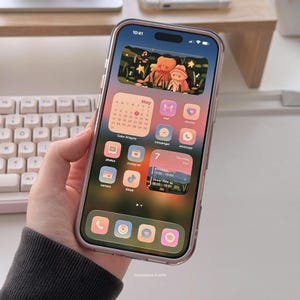 May include: A smartphone with a clear case displaying a custom home screen with a May calendar, app icons, and a background image of two teddy bears. The phone is held in a hand, with a keyboard visible in the background. The time is 10:41.