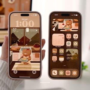 May include: Two smartphones displaying a custom digital interface with a brown and beige color palette. The screens feature illustrations of a brown bear character in a kitchen setting, integrated calendar widgets, and various app icons.