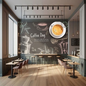 May include: Interior of a coffee shop with a chalkboard wall featuring coffee-related illustrations and the text "Coffee Day." Tables and chairs are arranged in the space, with a large window and track lighting. A cup of coffee is on a white plate.