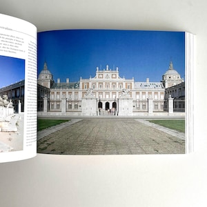 May include: A photograph of a book spread featuring a large, ornate palace with a symmetrical facade, set against a clear blue sky. The palace has multiple levels, columns, and domes. A paved pathway leads to the entrance.