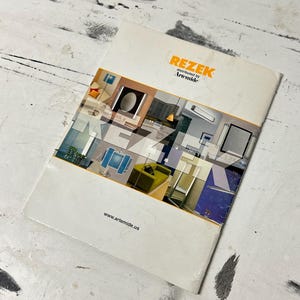 May include: A white brochure with the word "REZEK" in orange and the text "distributed by Artemide" in black. The brochure features a colorful interior design image and the website address www.artemide.us.