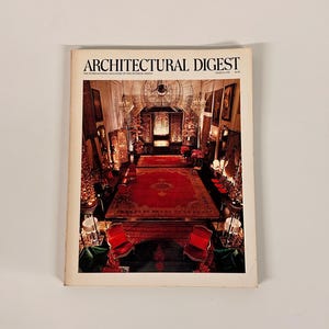 May include: A vintage Architectural Digest magazine cover featuring a detailed interior design scene. The cover displays the magazine's title and a photograph of a room with a large red rug, red chairs, and ornate decor.