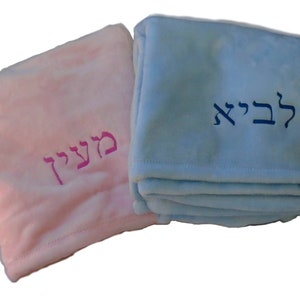 May include: Two personalized baby blankets, one pink with the Hebrew word "Meirav" embroidered in pink, and one light blue with the Hebrew word "Levi" embroidered in blue.