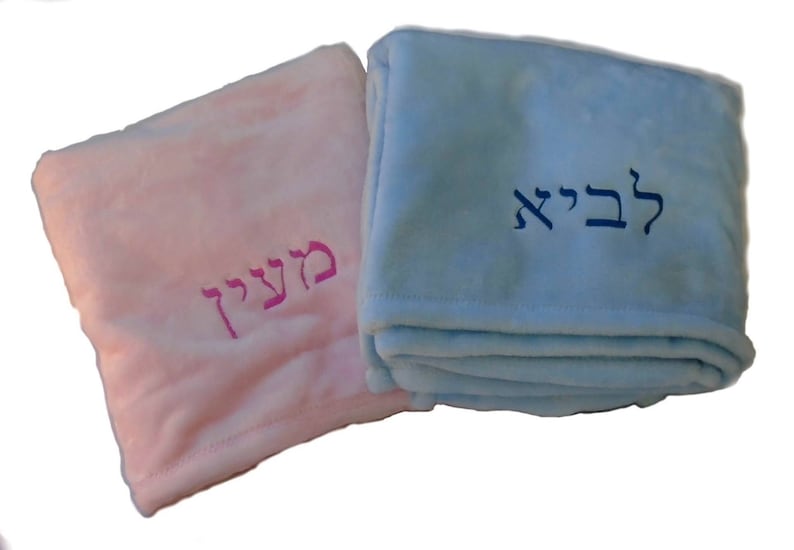 May include: Two personalized baby blankets, one pink with the Hebrew word "Meirav" embroidered in pink, and one light blue with the Hebrew word "Levi" embroidered in blue.