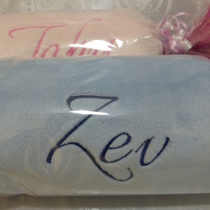 May include: Two personalized baby blankets, one pink with the name "Talia" embroidered in pink and one light blue with the name "Zev" embroidered in dark blue.