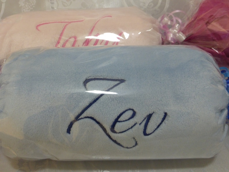 May include: Two personalized baby blankets, one pink with the name "Talia" embroidered in pink and one light blue with the name "Zev" embroidered in dark blue.