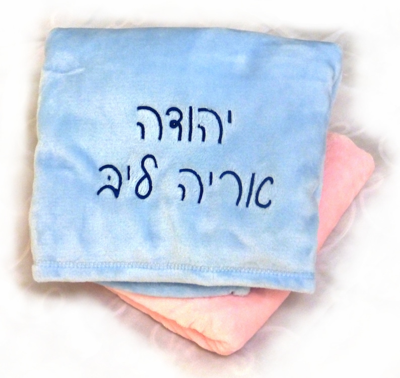 May include: A light blue and pink baby blanket with the Hebrew text "Y'rodeh" and "O'ri'eh 8'im" embroidered in dark blue.