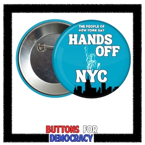 May include: A round, blue button with the text "HANDS OFF NYC" and an image of the Statue of Liberty. The button also has the text "THE PEOPLE OF NEW YORK SAY" and a black silhouette of the NYC skyline. The button is made of metal.