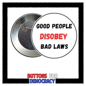 May include: A round, silver-colored button with the text "GOOD PEOPLE DISOBEY BAD LAWS" in black and red. The button has a pin on the back and is framed by a black border. The words "BUTTONS FOR DEMOCRACY" are at the bottom.