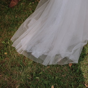 May include: A white tulle wedding dress train with lace detailing, lying on green grass.