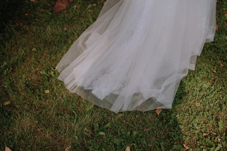 May include: A white tulle wedding dress train with lace detailing, lying on green grass.