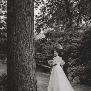 May include: A bride and groom walking down a path in a forest. The bride is wearing a white wedding dress and carrying a bouquet of flowers. The groom is wearing a suit and tie.