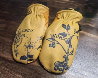 May include: A pair of yellow leather mittens with black floral and hummingbird designs. The word "KINCO" is printed on each mitten. The mittens are designed for outdoor work and protection.