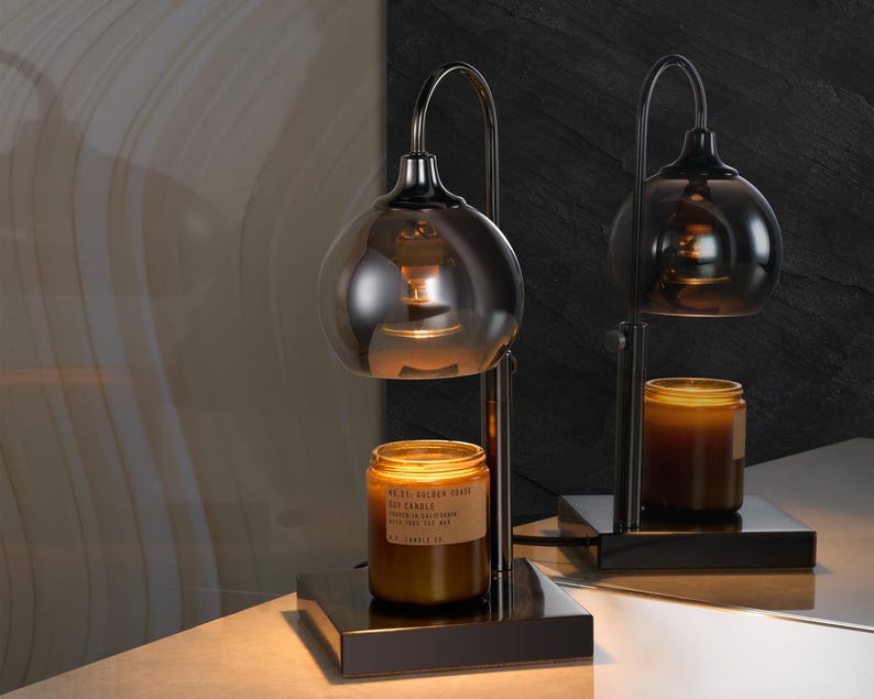 Puede incluir: Un calentador de velas de metal negro con una pantalla de vidrio y un tarro de vidrio marr&oacute;n con una vela. La vela est&aacute; etiquetada "VOLUSPA JAPANESE  CEREAL  SOY CANDLE  PEACH & NECTARINE  FRAGRANCE OIL  3.7 OZ (105G)".