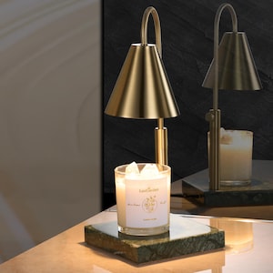 May include: A gold metal candle warmer with a green marble base and a white candle with the text "Luxe Garden" on the label. The candle warmer has a cone-shaped shade.