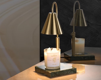 May include: A gold metal candle warmer with a green marble base and a white candle with the text "Luxe Garden" on the label. The candle warmer has a cone-shaped shade.