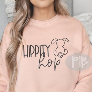 Może przedstawiać: Różowa bluza z nadrukiem "Hippity Hop" i kreskówkowym królikiem.