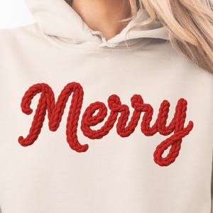 Puede incluir: Sudadera con capucha de color crema con la palabra "Merry" en letras rojas y audaces con forma de cuerda en el pecho. El diseño festivo es perfecto para la temporada navideña. La sudadera tiene una capucha con cordón y un bolsillo de canguro.