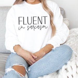 May include: White sweatshirt with the text "FLUENT in sarcasm" printed on the front.