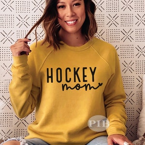 May include: A mustard yellow sweatshirt with black text that reads "HOCKEY mom" with a small heart after the word "mom".