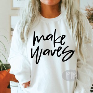 May include: White sweatshirt with the text "make waves" in black script lettering.