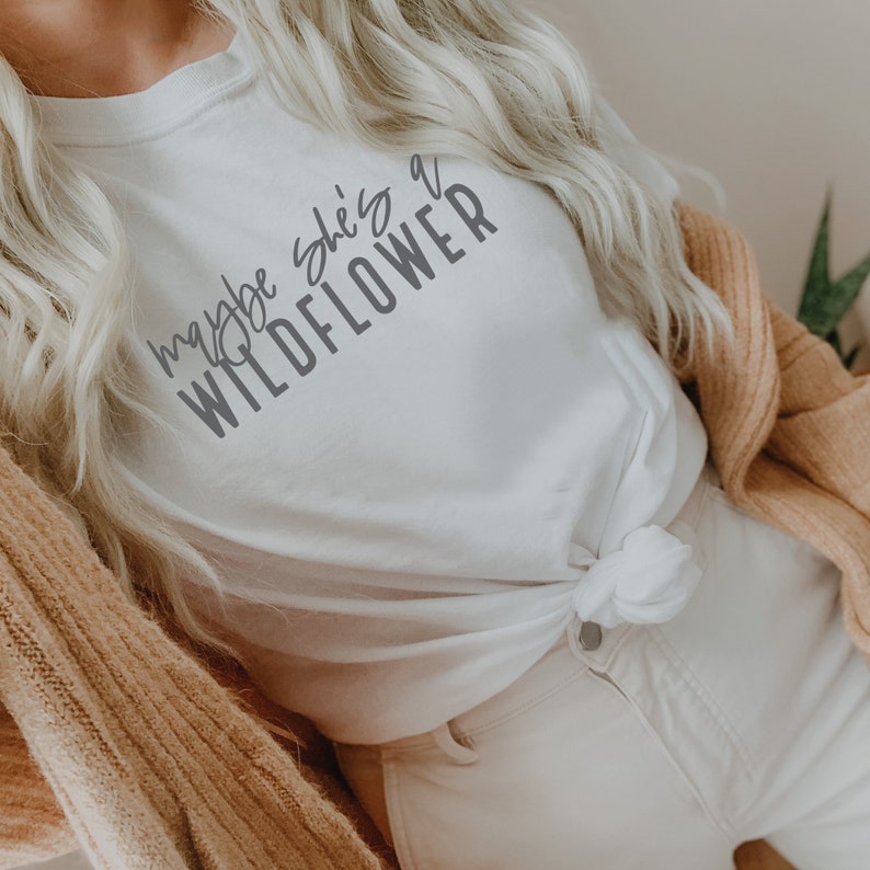 May include: White t-shirt with the text "maybe she's a wildflower" in gray lettering.