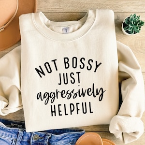 May include: A cream-coloured sweatshirt with the text "Not bossy just aggressively helpful" printed in black.