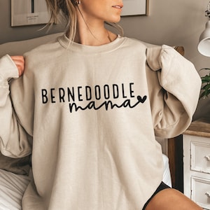 May include: A beige sweatshirt with the text "BERNEDoodle mama" in black lettering with a small black heart.
