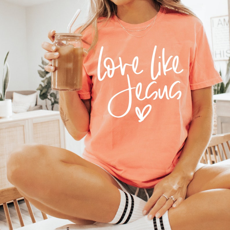 May include: A coral colored t-shirt with the text 'love like Jesus' in white lettering with a small heart below the text.