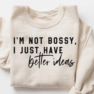 Op de afbeelding: Een crèmekleurige sweatshirt met de zwarte tekst "I'M NOT BOSSY, I JUST HAVE better ideas". De sweatshirt heeft een ronde hals en lange mouwen, ideaal voor casual wear.