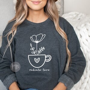 May include: A dark gray sweatshirt with a white graphic of a flower in a coffee cup with a heart. The text "radiate love" is below the graphic.