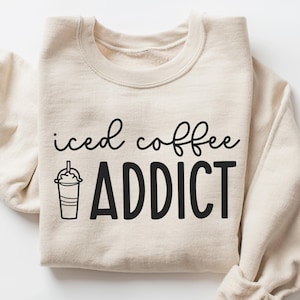 May include: A beige sweatshirt with the text "iced coffee ADDICT" in black lettering. A black and white illustration of a cup of iced coffee is to the left of the text.