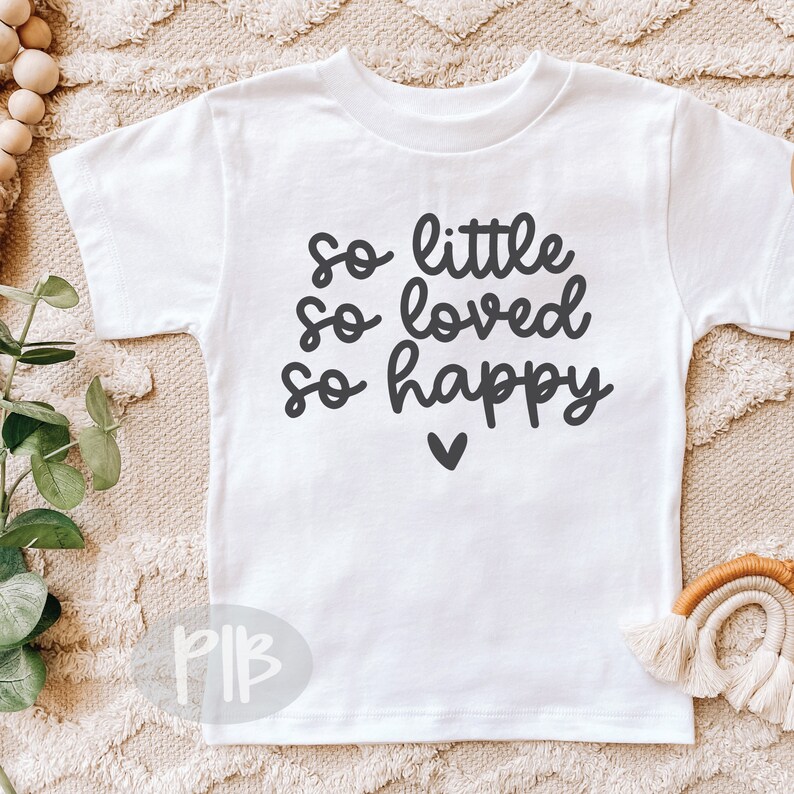 Puede incluir: Un body blanco para beb&eacute; con texto negro que dice "so little so loved so happy" con un peque&ntilde;o coraz&oacute;n debajo del texto.