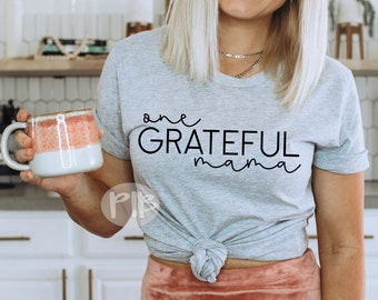 May include: A gray t-shirt with the text "one GRATEFUL mama" printed in black. The shirt is being worn by a person holding a mug.