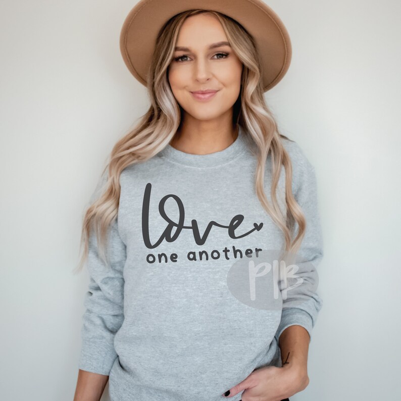 May include: A light gray sweatshirt with the words "Love one another" in black script. The word "Love" has a small heart replacing the "o". The sweatshirt is long-sleeved and has a crew neck.