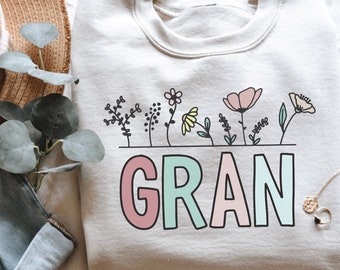 May include: A light grey sweatshirt with the word "GRAN" in colourful letters and a row of flowers above the word.