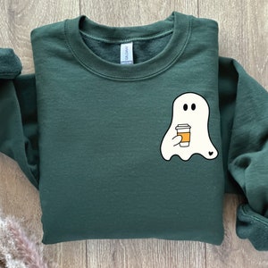 May include: A dark green sweatshirt with a white ghost holding a cup of coffee. The ghost has two eyes and a small heart on its side.