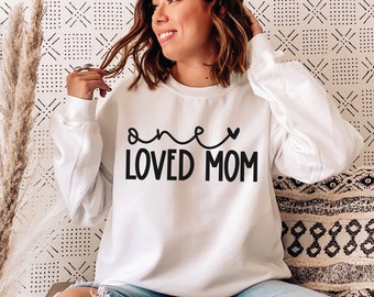 May include: White sweatshirt with black text that reads "one loved mom" with a heart symbol.